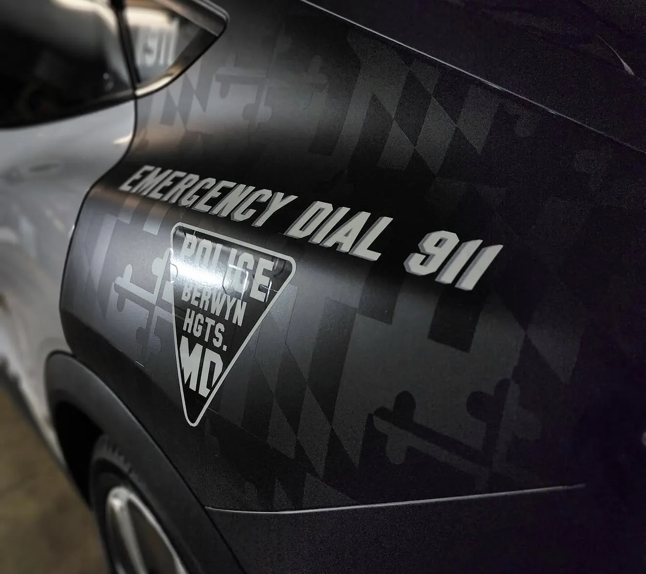 Close-up of a Berwyn Heights police SUV rear quarter with EMERGENCY DIAL 911 lettering and a triangle department decal
